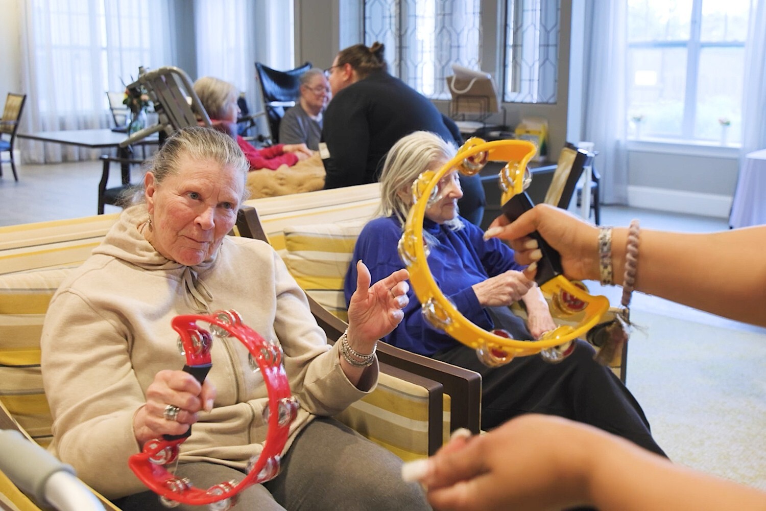 Residents at Arbor Terrace Glenview senior living join in a cheerful music activity, playing tambourines together as part of the active senior lifestyle Glenview offers.
